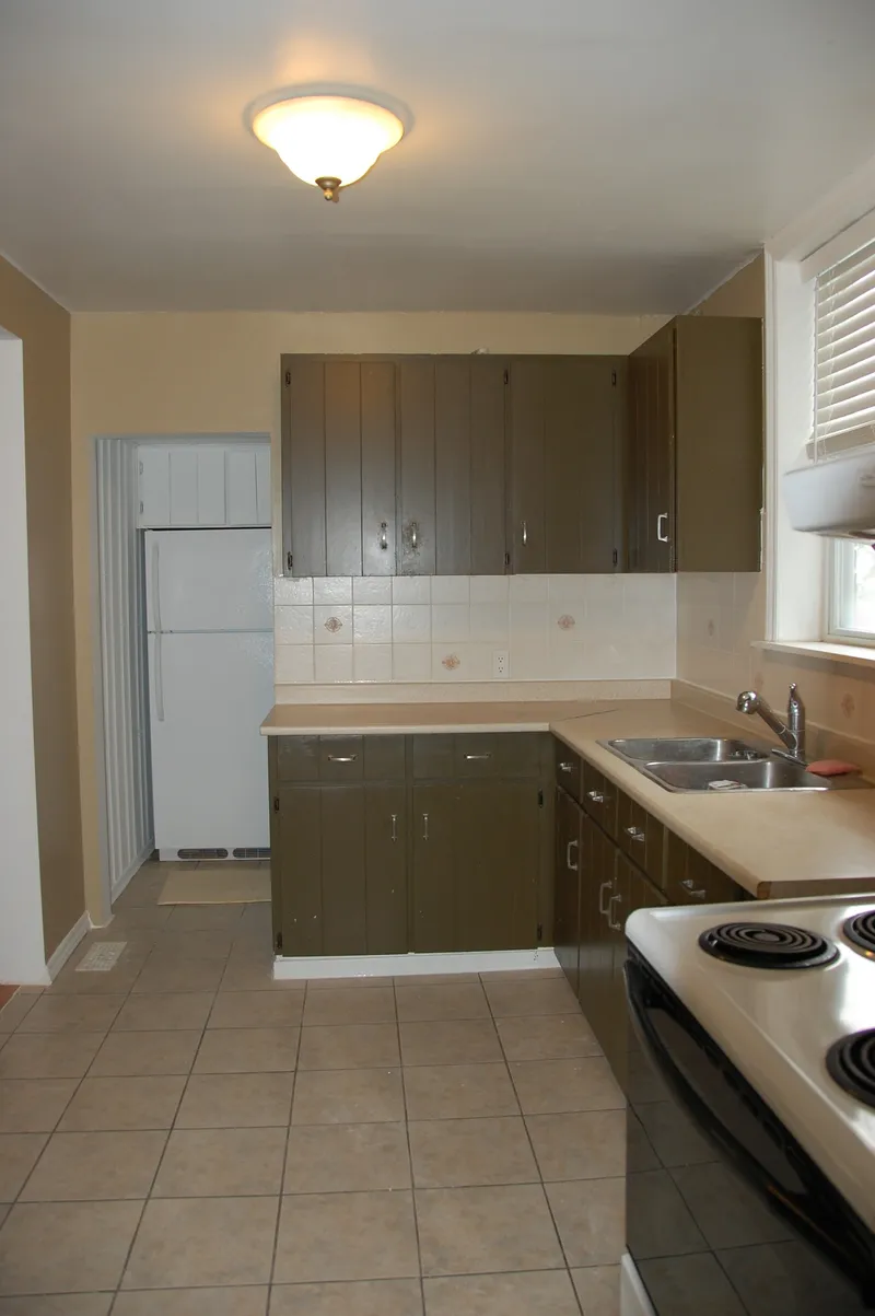 Before: another view along the original kitchen, with darker cabinetry, the range in the foreground and the refrigerator at the far end.