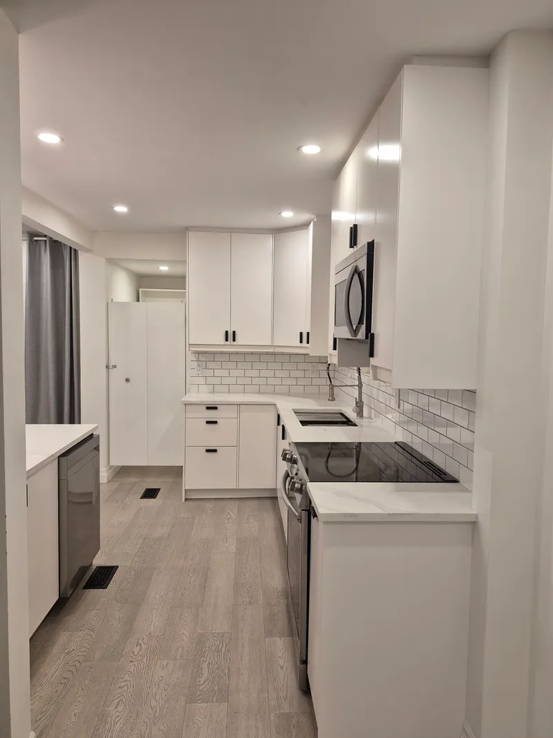 After: another view along the renovated kitchen, with white cabinetry, a cooktop and dishwasher, and updated surfaces.