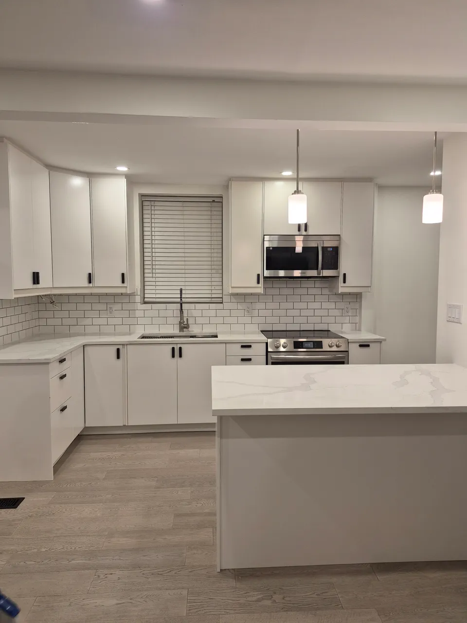 After: renovated kitchen with white cabinetry, black hardware, a tiled backsplash, peninsula and pendant lighting.