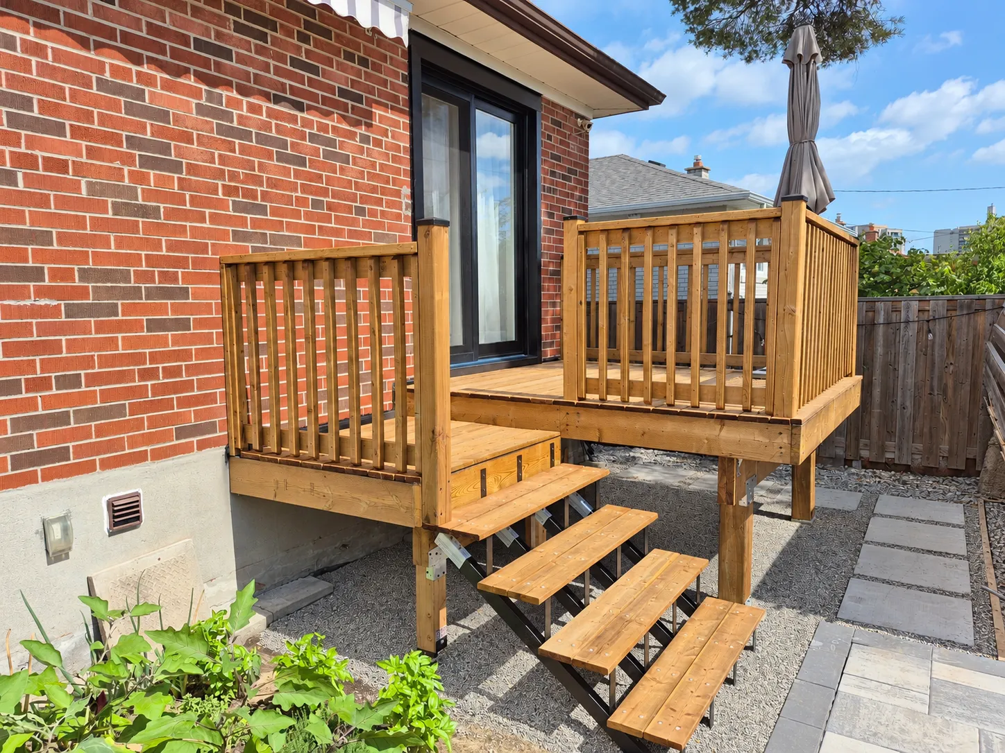 Rebuilt backyard wood deck with railings and a new staircase against a brick house.