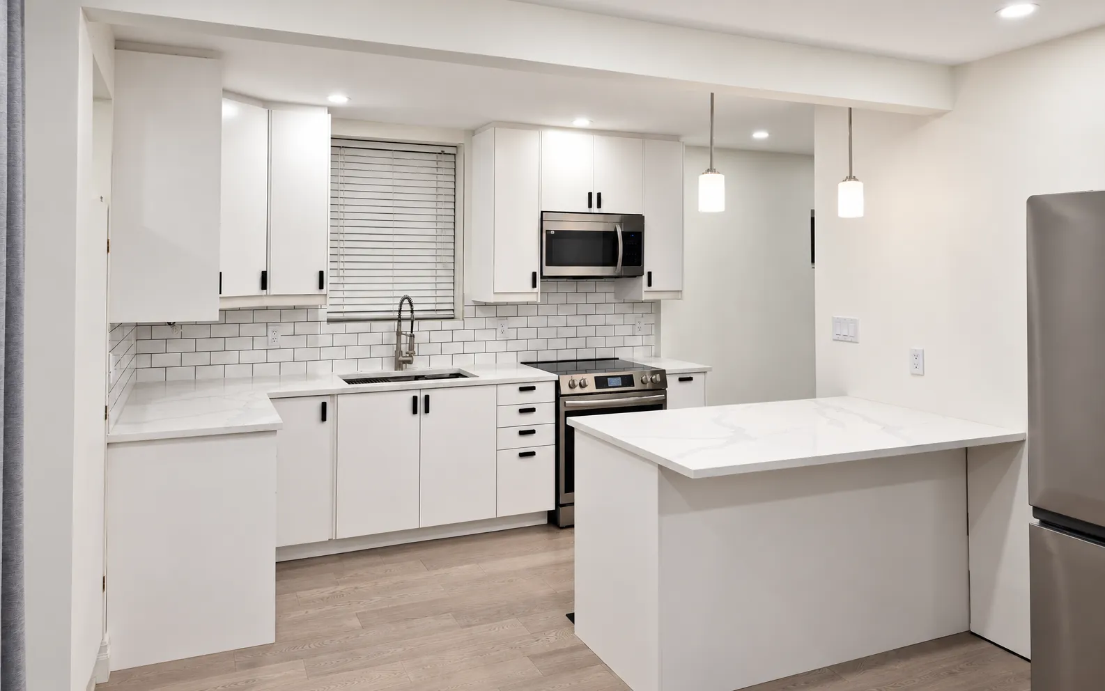 Renovated kitchen with white shaker cabinets, subway-tile backsplash, quartz peninsula and pendant lighting.